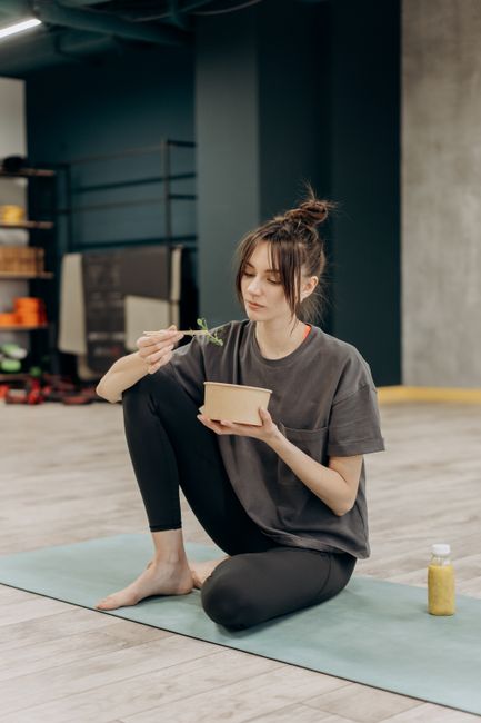 Woman practicing yoga outdoors surrounded by plants and healthy food