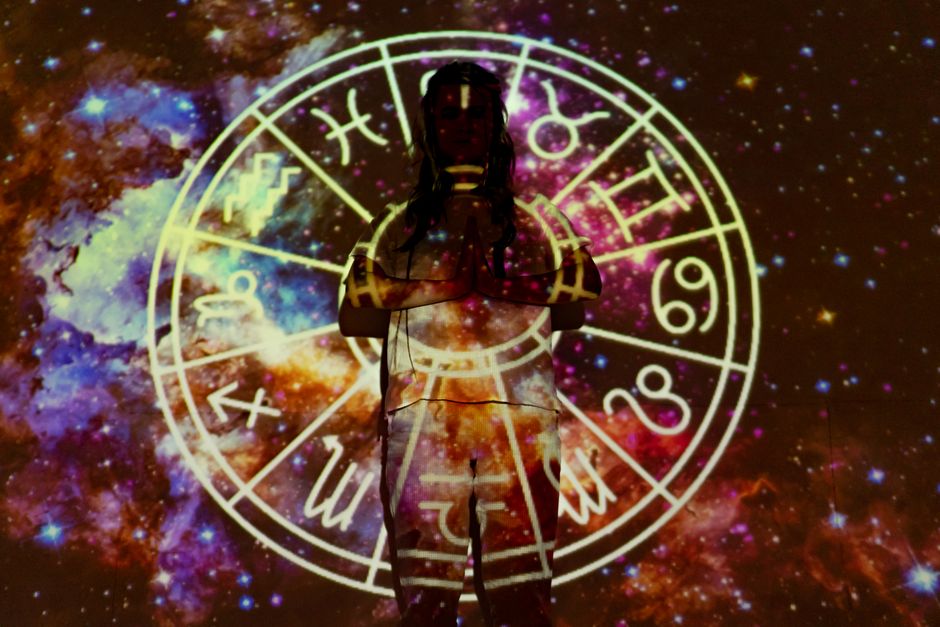 Person meditating under stars with astrological symbols